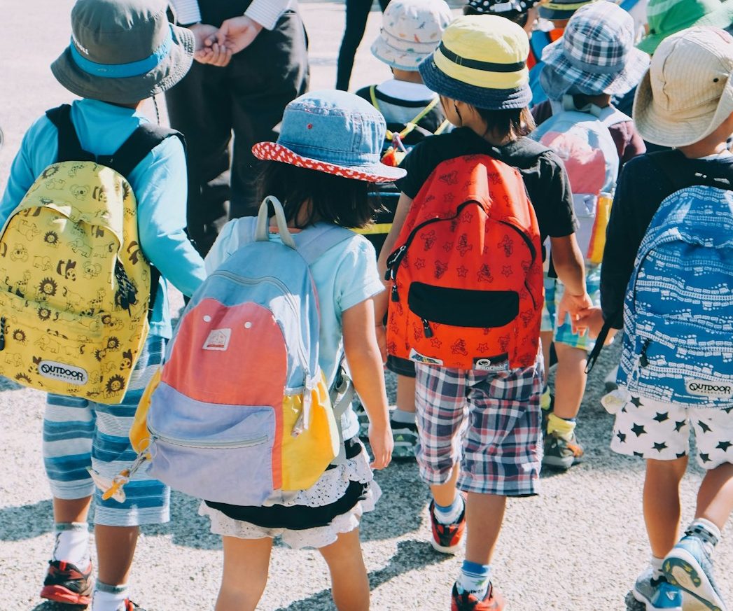 group of people wearing white and orange backpacks walking on gray concrete pavement during daytime